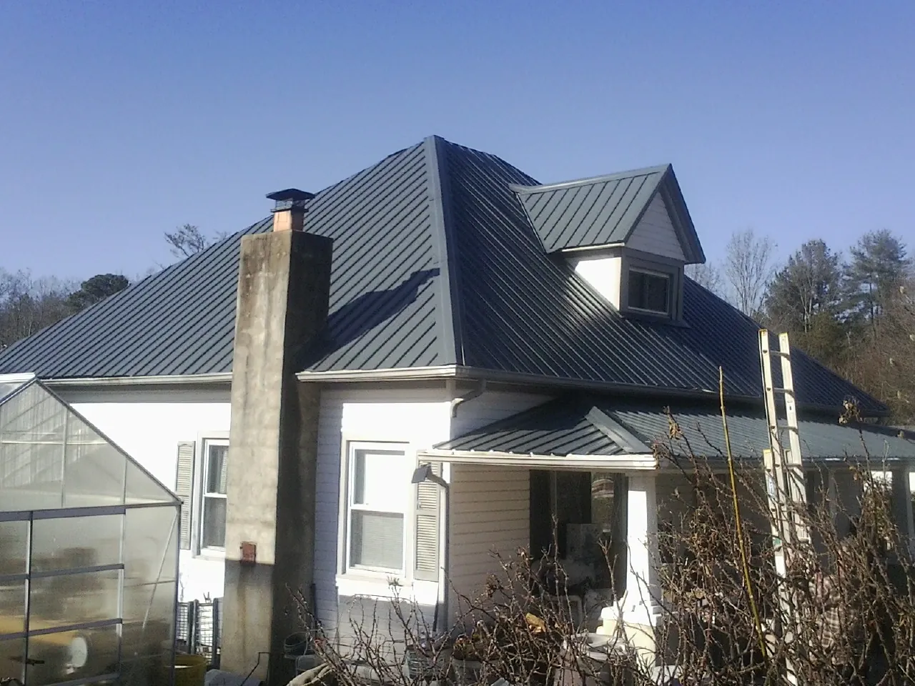 Dark blue standing seam metal roof on a white farmhouse with dormer — Slate & Tile Roof Repair by Roofing Brothers in Sallisaw