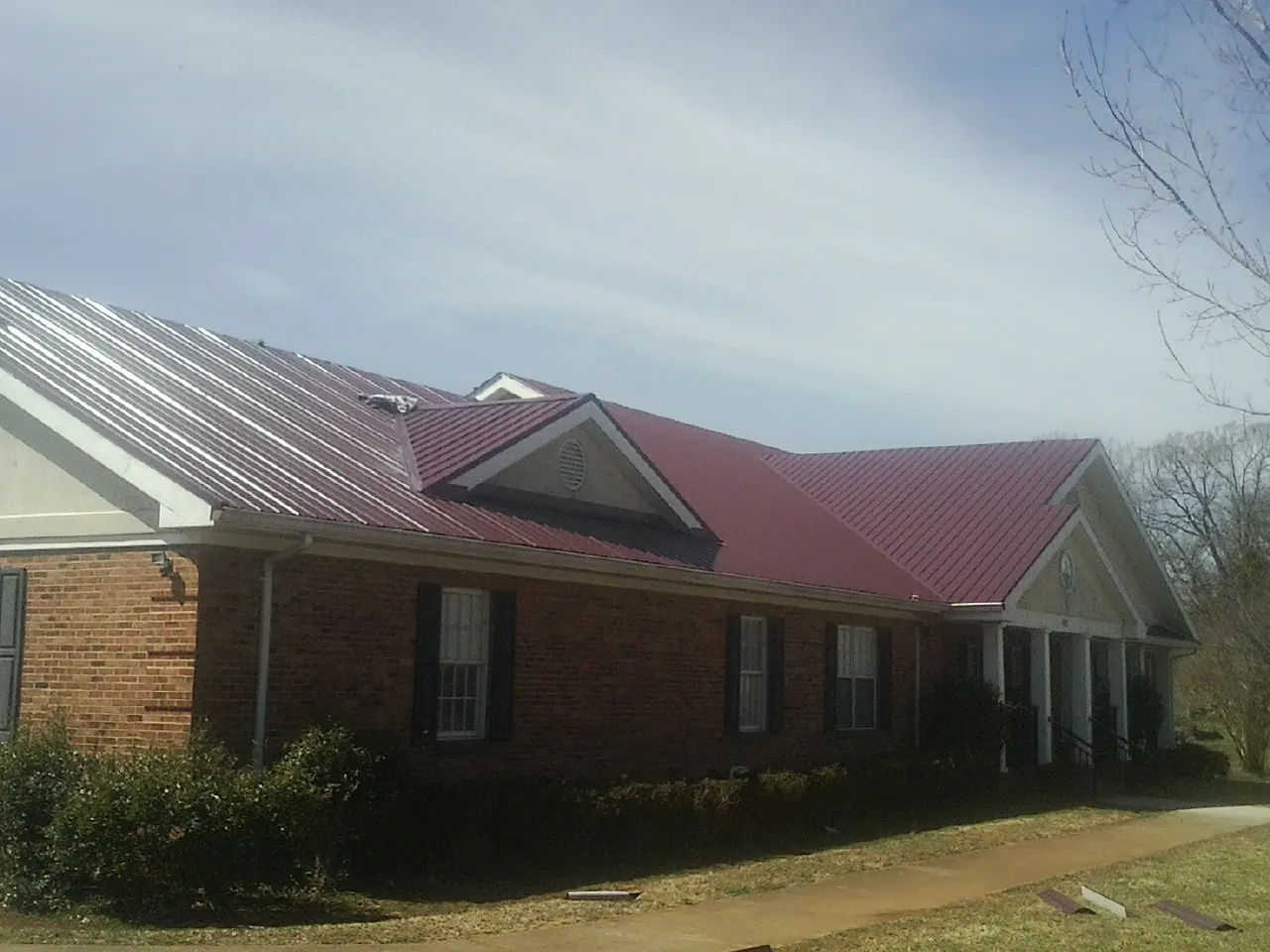 Red metal roof with gabled entries on a long brick building, from a Hail Damage Roof Repair job in Sallisaw