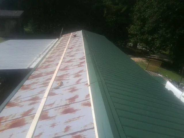 Old rusted panels beside newly installed green metal roofing — Wind Damage Roof Repair by Roofing Brothers in Sallisaw