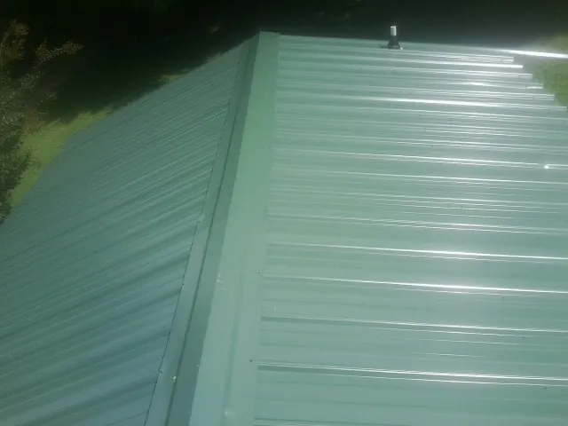 New green metal panels meeting at the ridge of a roof — Flat Roof Repair work by our crew in Sallisaw