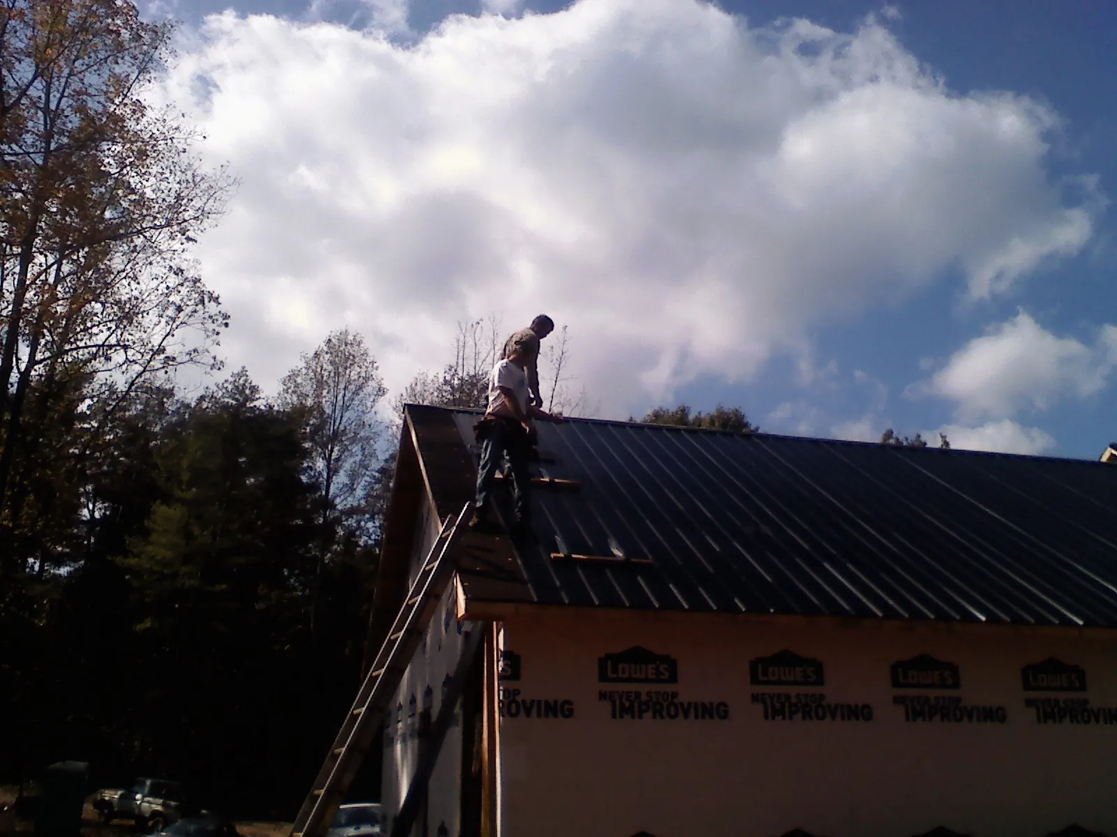 Roofer fastening dark metal panels high against a cloudy sky, from a Roof Inspection job in Sallisaw