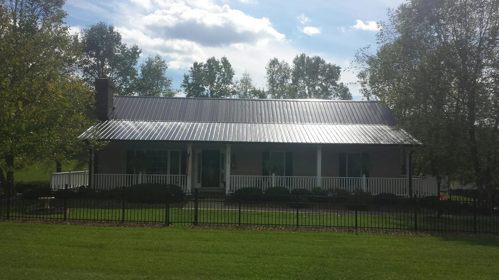 Gray metal roof on a brick ranch with a full width front porch — Gutter Guard Installation work by our crew in Sallisaw