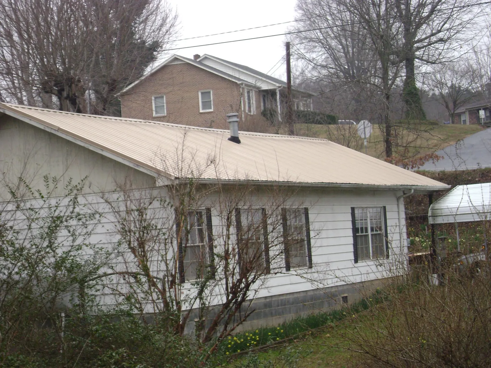 Tan metal roof on a white sided house set into a hillside — Commercial Roofing by Roofing Brothers in Sallisaw