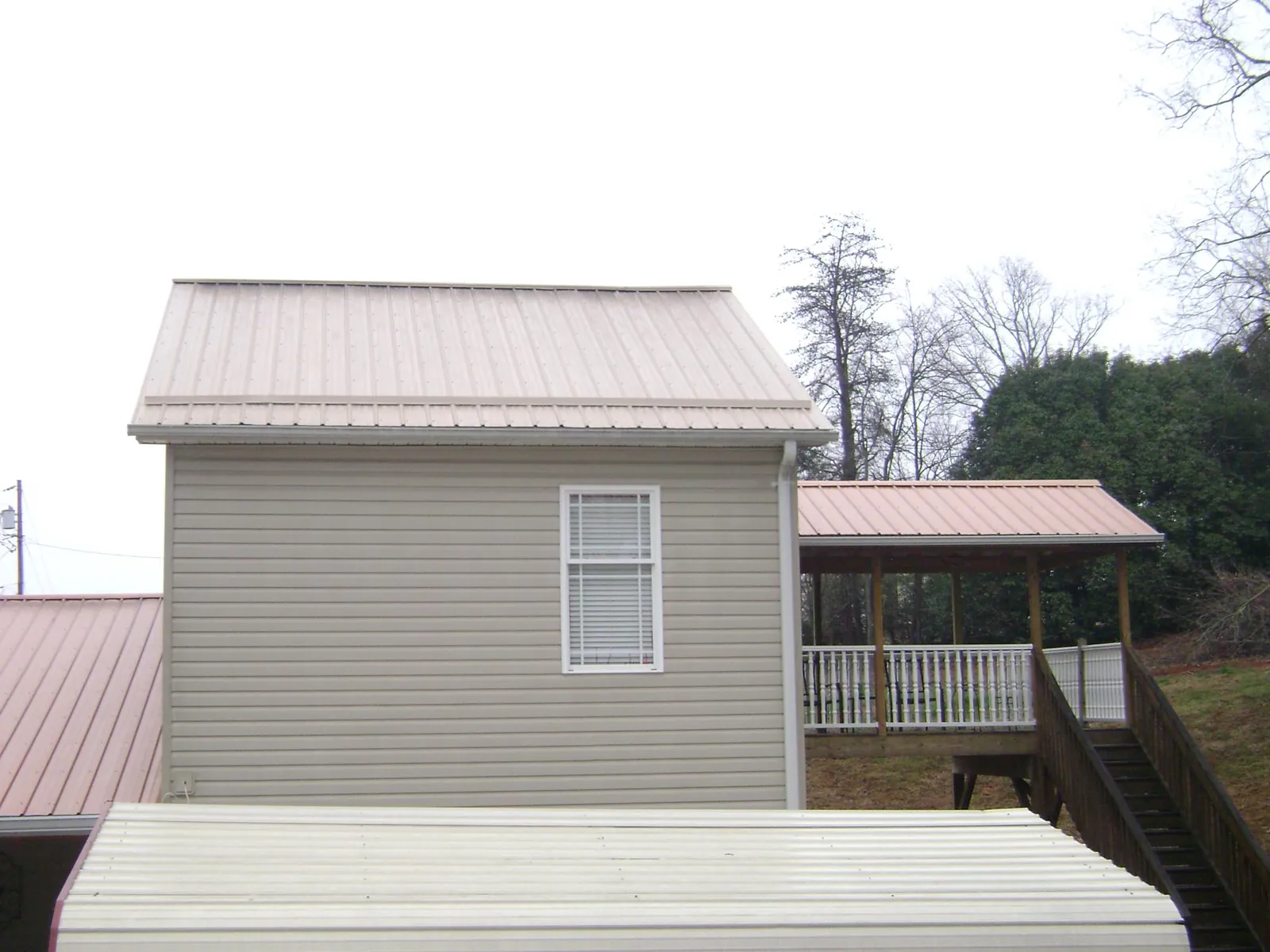 Tan metal roofs on a two story addition and attached porch, from a Roof Replacement job in Sallisaw
