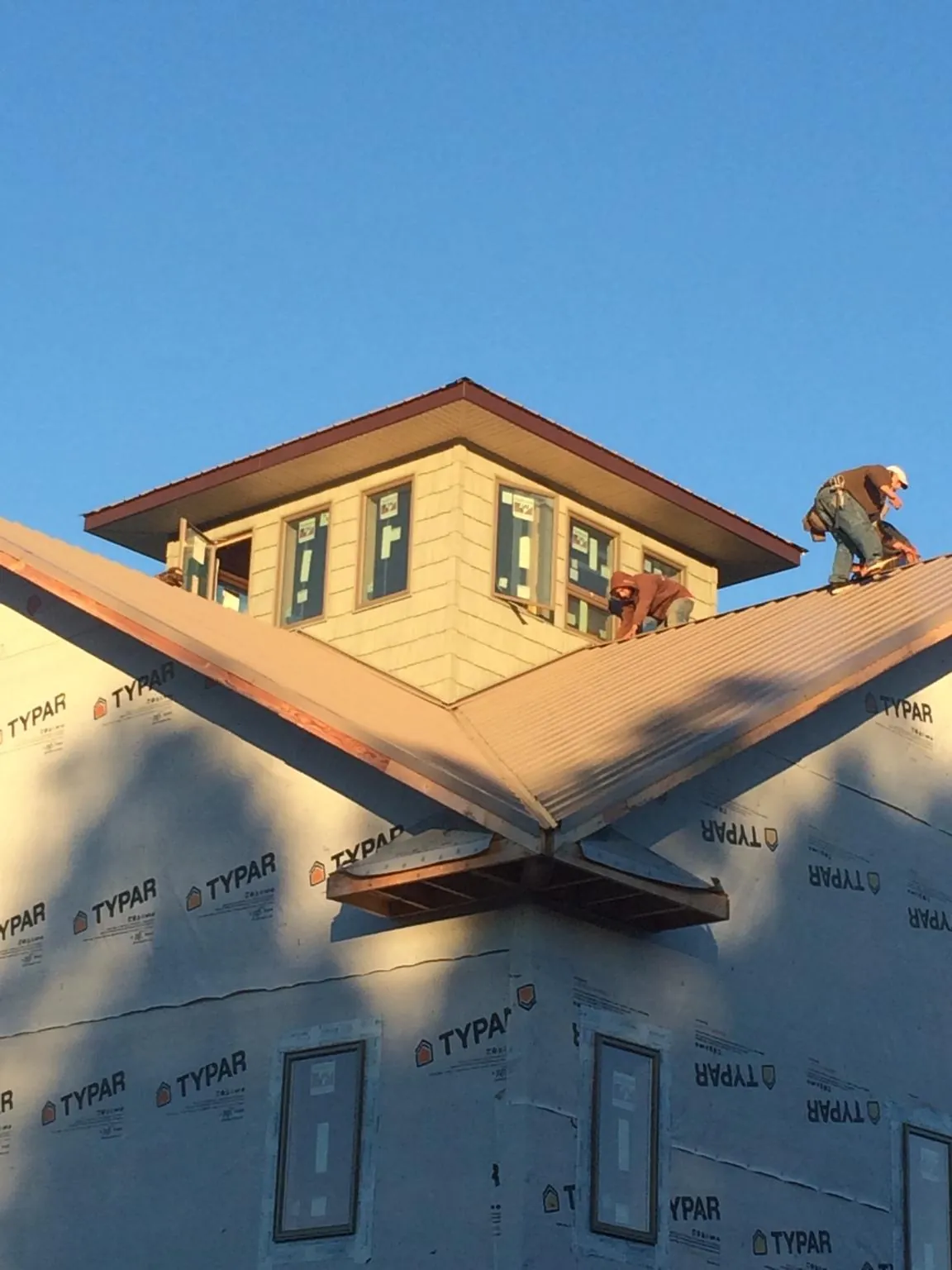 Roofers working around a rooftop cupola on a new metal roof at sunset — Roof Waterproofing in Sallisaw by Roofing Brothers